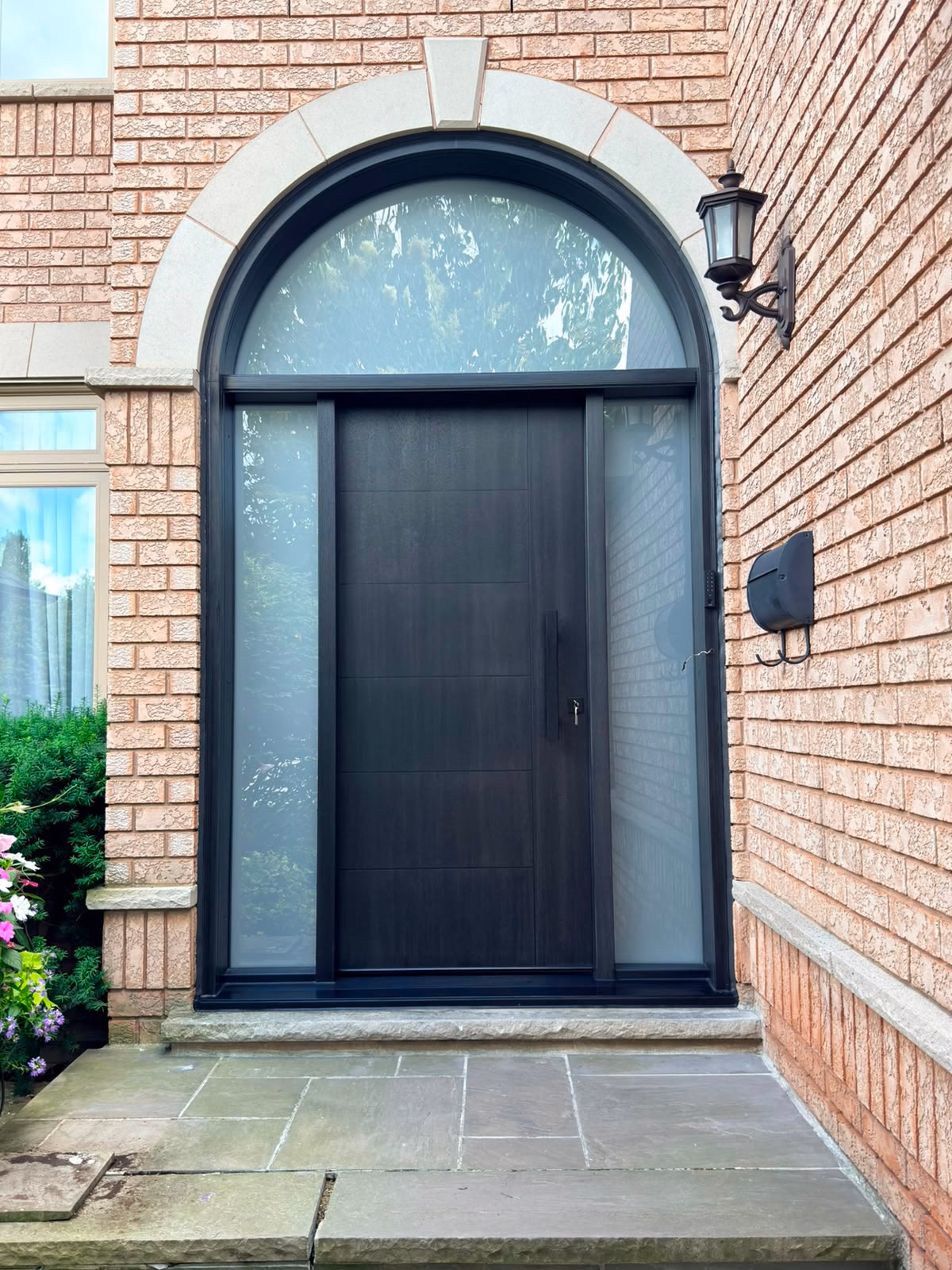 Black entry door with wide glass sidelights and a large arched transom