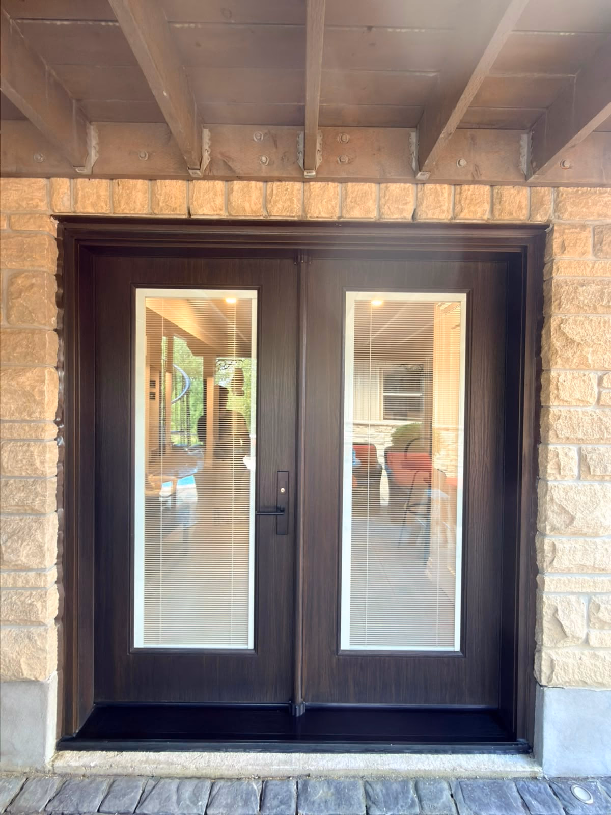 Dark double entry doors with tall glass panels beneath a covered entry